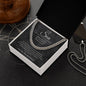 Charcoal script card and Cuban link chain in open gift box on a dark compass-print surface beside a dog tag