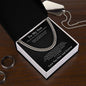 Cuban link chain gift for son from Mom in open box on wood table, silver dog tag and dark rings nearby