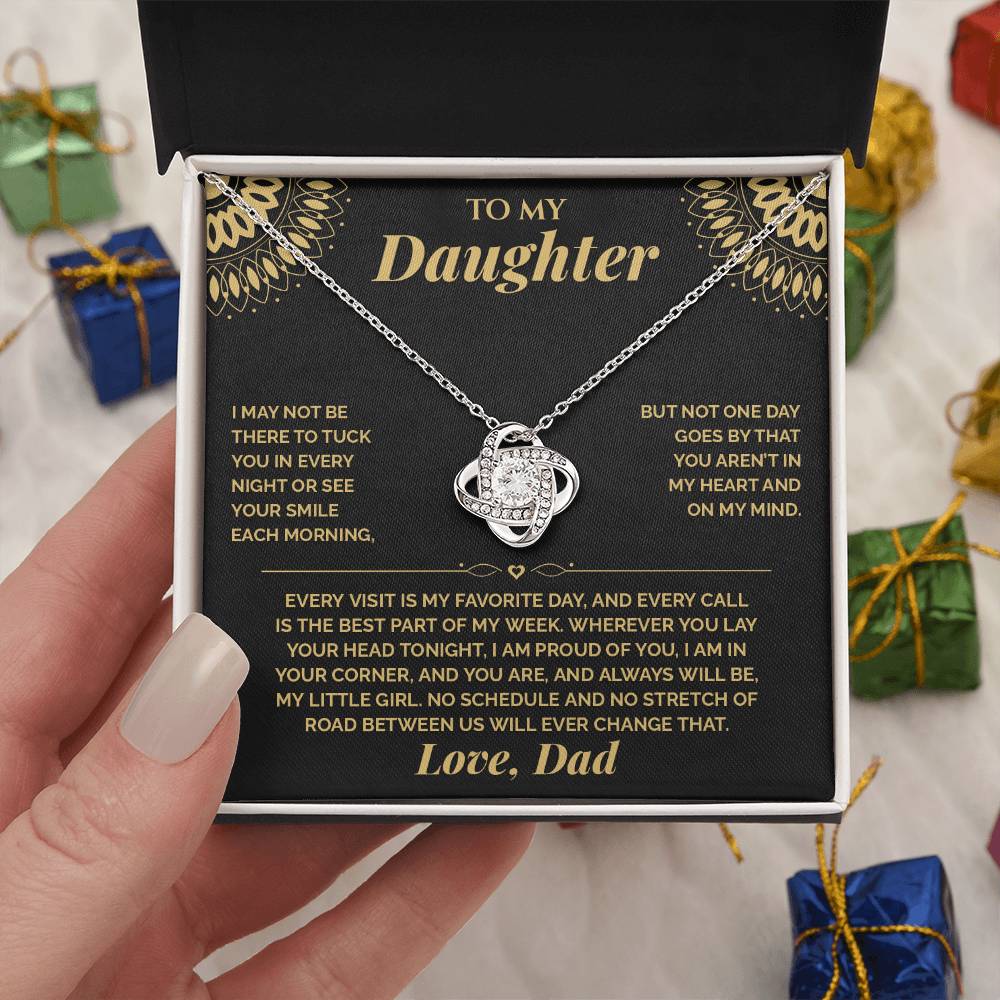 Hand holding the black and gold To My Daughter card from Dad and Love Knot necklace box among wrapped Christmas gifts