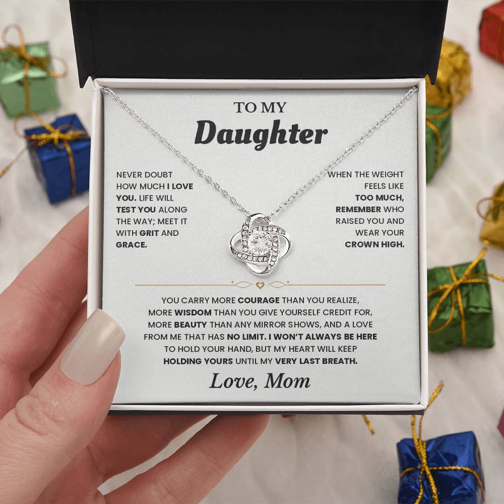 Hand holding the white To My Daughter card from Mom and Love Knot necklace box among wrapped Christmas gifts