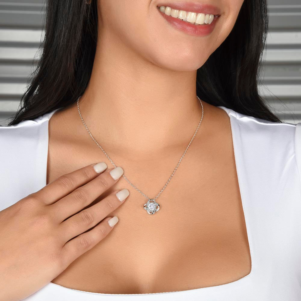 Smiling woman touching the Love Knot pendant at her neckline
