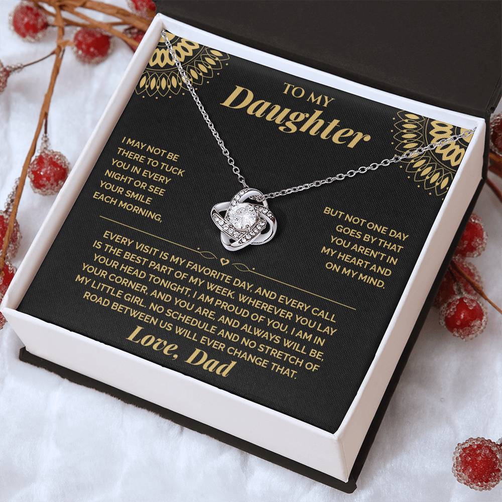 Tilted white gift box holding the black and gold To My Daughter card from Dad and Love Knot necklace among red berries