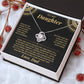 Tilted white gift box holding the black and gold To My Daughter card from Dad and Love Knot necklace among red berries