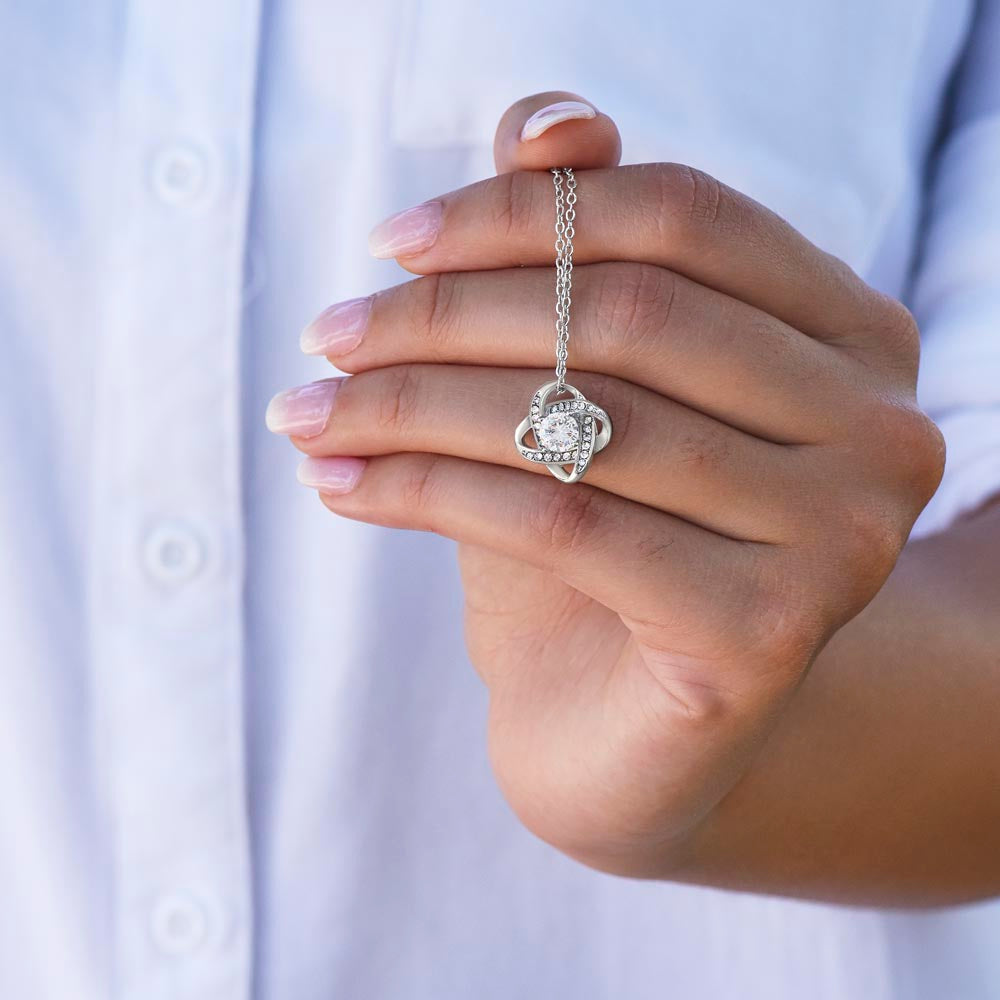 Hand holding the Love Knot pendant against a white top