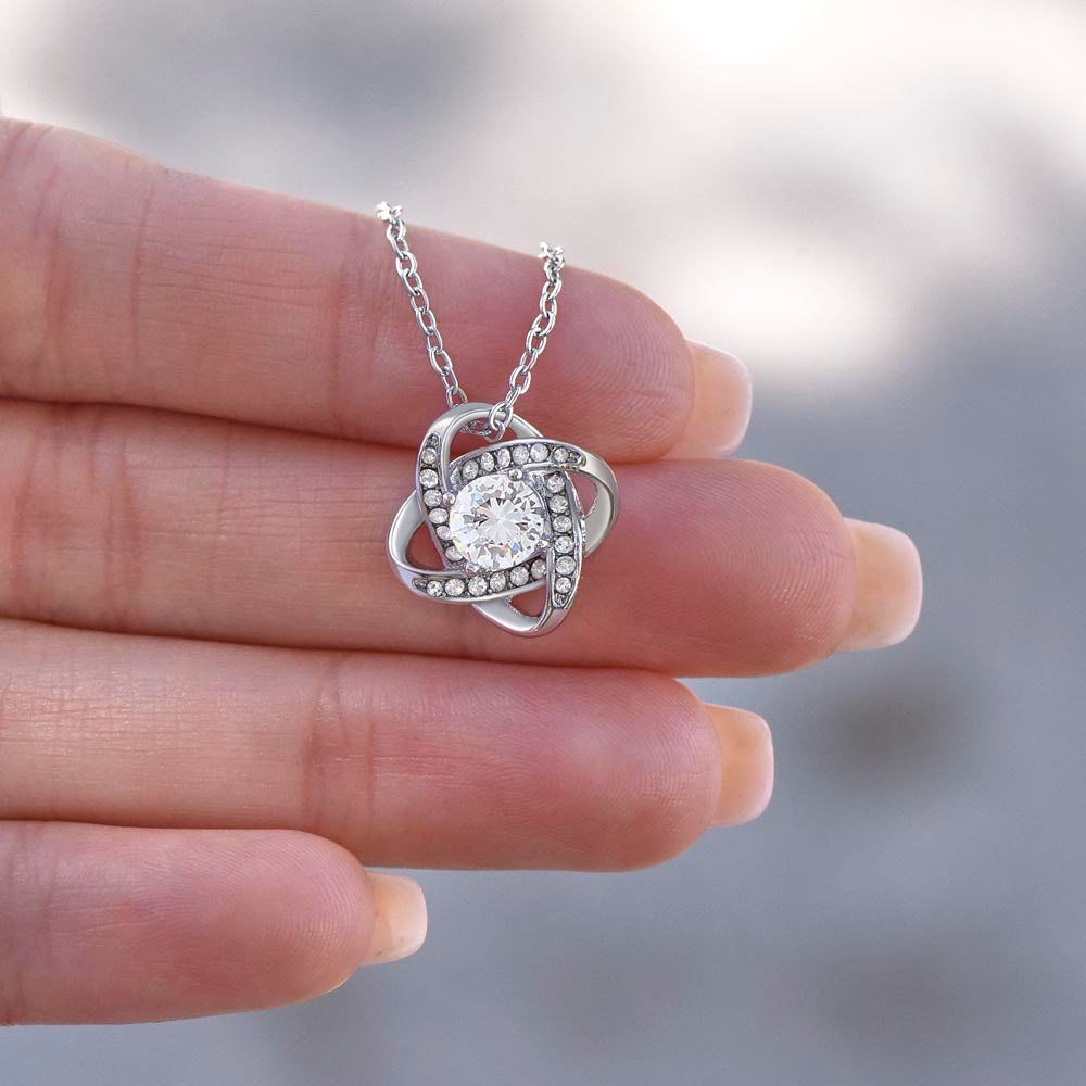 Love Knot pendant resting across fingers, showing the round center stone up close