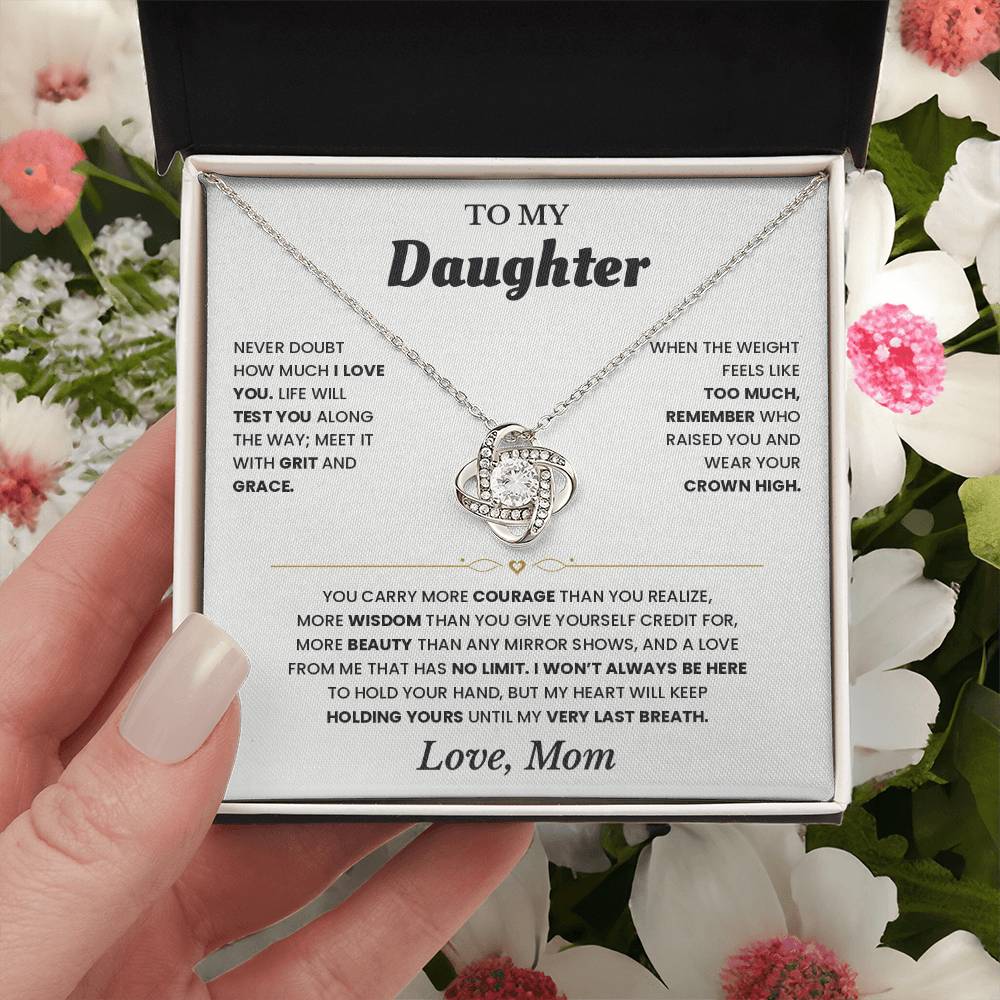 Hand holding the white To My Daughter card from Mom gift box among pink and white flowers