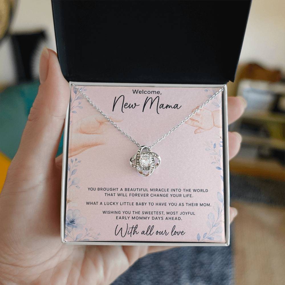 Hand holding open gift box with white gold Love Knot necklace and new mom message card