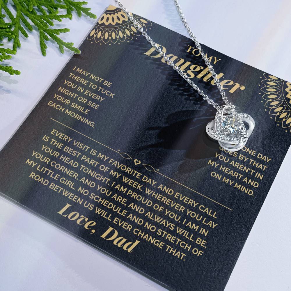 Black and gold To My Daughter card from Dad with the Love Knot necklace laid flat beside green leaves