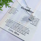 White To My Daughter card from Mom with the Love Knot necklace laid flat beside green leaves
