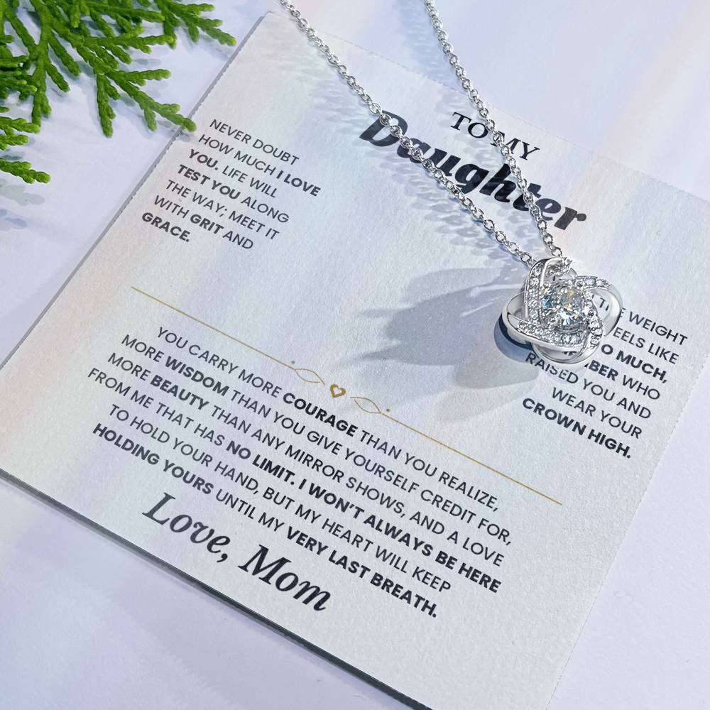 White To My Daughter card from Mom with the Love Knot necklace laid flat beside green leaves