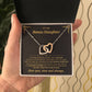 Hand presenting the open gift box with the black and gold To My Bonus Daughter card and two linked heart pendants