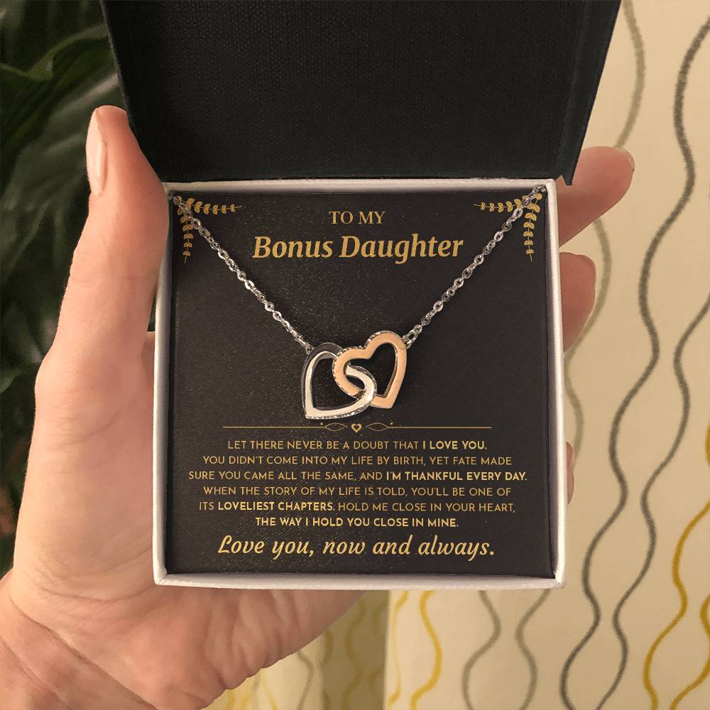 Hand presenting the open gift box with the black and gold To My Bonus Daughter card and two linked heart pendants