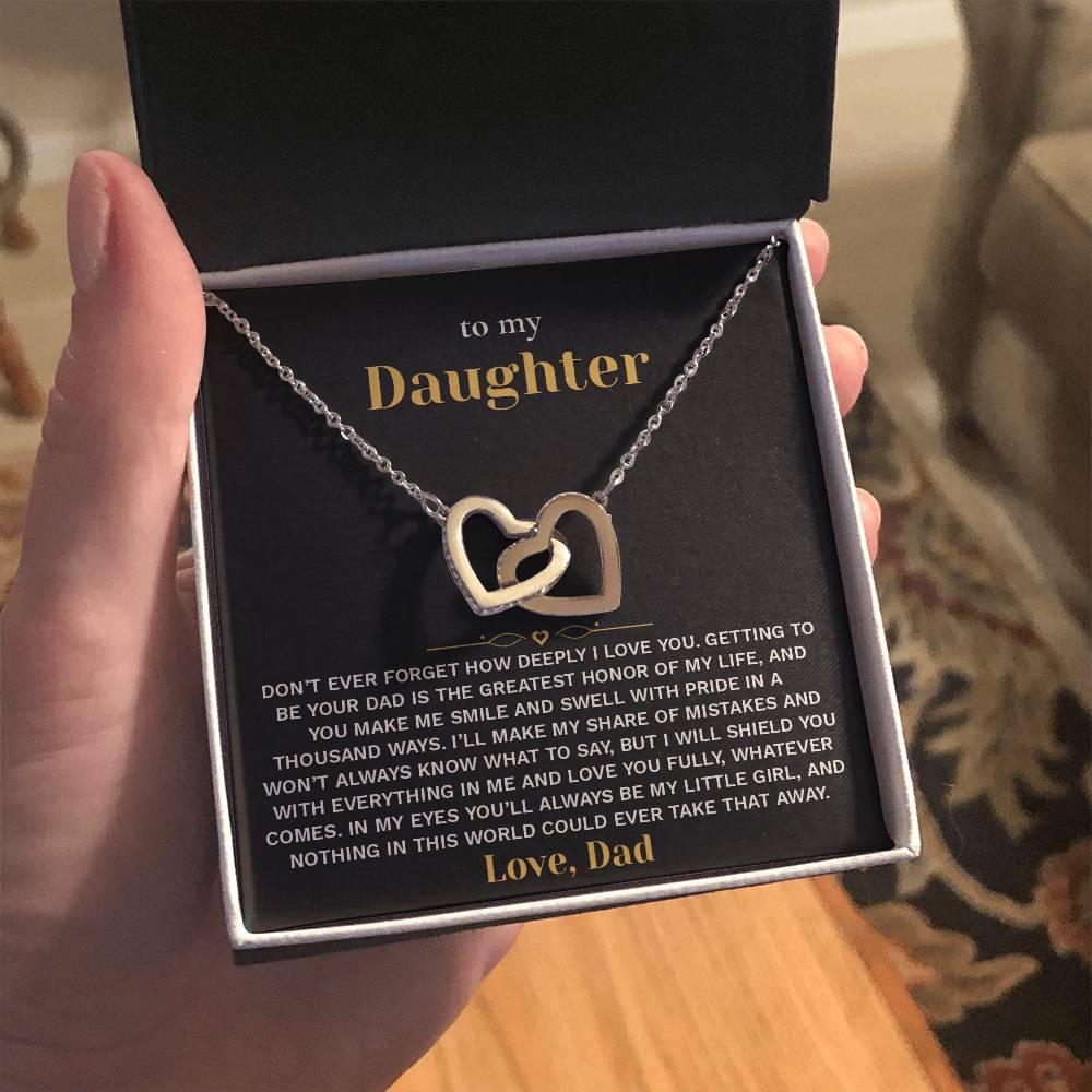 Open gift box with the black and gold To My Daughter card from Dad and Interlocking Hearts necklace held up indoors