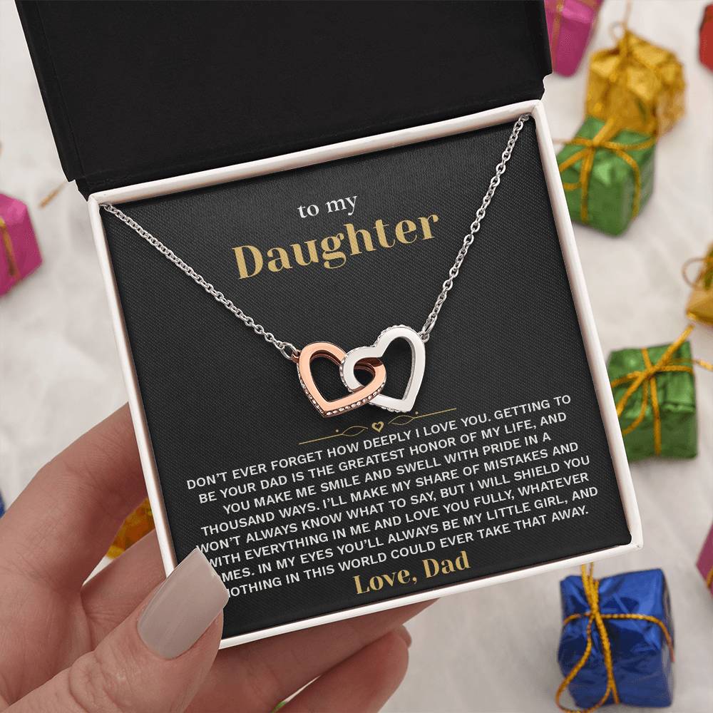 Hand holding the black and gold To My Daughter card from Dad and linked hearts necklace box among wrapped Christmas gifts