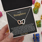 Hand holding the black and gold To My Daughter card from Dad and linked hearts necklace box among wrapped Christmas gifts