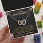 Hand holding the black and gold To My Bonus Daughter card and linked hearts necklace box among wrapped Christmas gifts