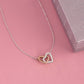 Interlocking Hearts necklace on a pink surface beside a pink gift box