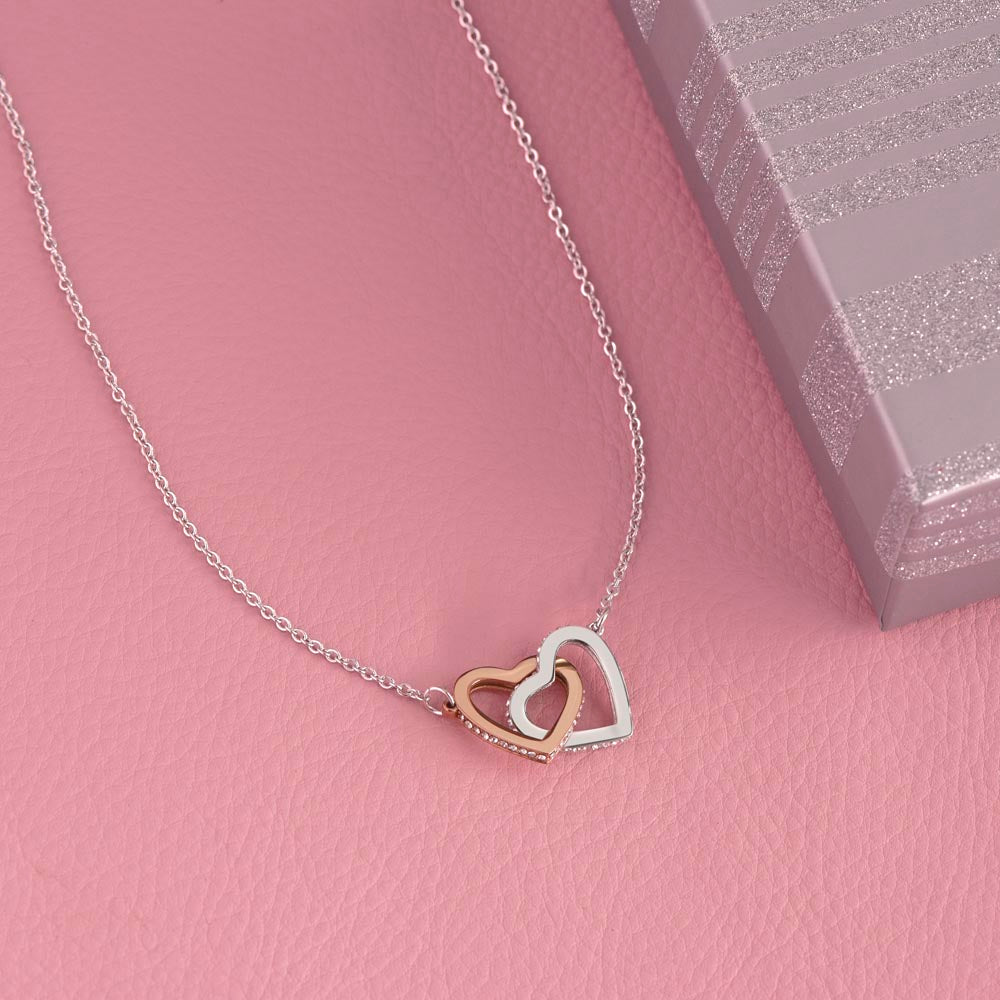 Interlocking Hearts necklace on a pink surface beside a pink gift box