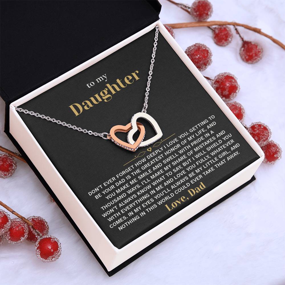 Tilted white gift box holding the black and gold To My Daughter card from Dad and Interlocking Hearts necklace among red berries and pinecones