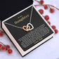 Tilted white gift box holding the black and gold To My Daughter card from Dad and Interlocking Hearts necklace among red berries and pinecones