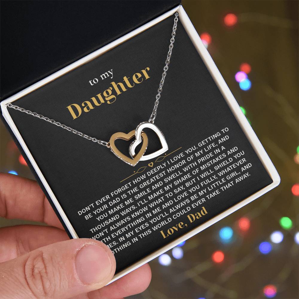 Hand holding the black and gold To My Daughter card from Dad gift box in front of glowing holiday lights