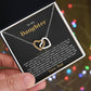 Hand holding the black and gold To My Daughter card from Dad gift box in front of glowing holiday lights