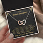 Hand holding an open black gift box with the black and gold To My Bonus Daughter card and linked hearts necklace beside a knit blanket