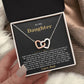 Hand holding an open black gift box with the black and gold To My Daughter card from Dad and linked hearts necklace beside a knit blanket