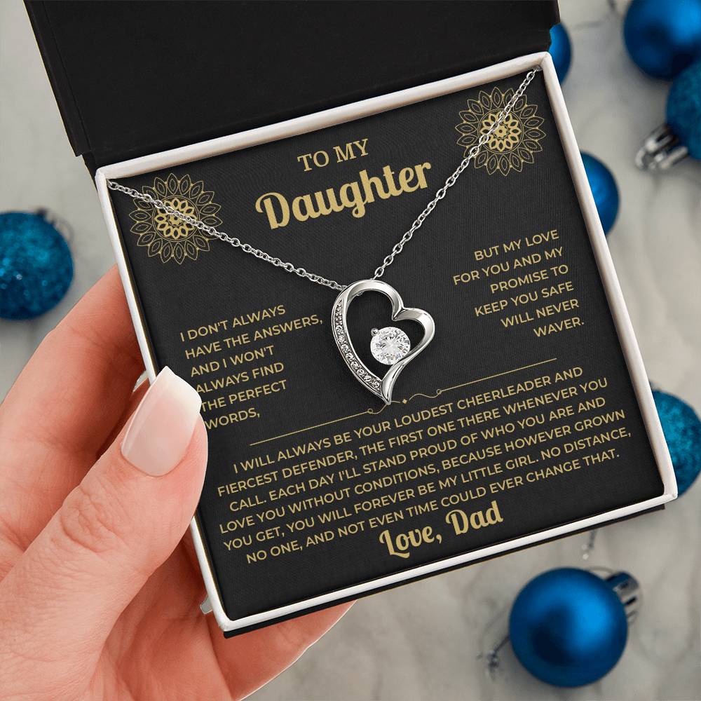 Hand holding the black and gold To My Daughter card from Dad gift box by blue Christmas ornaments on white fur
