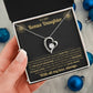 Hand holding the black and gold To My Bonus Daughter card gift box by blue Christmas ornaments on white fur