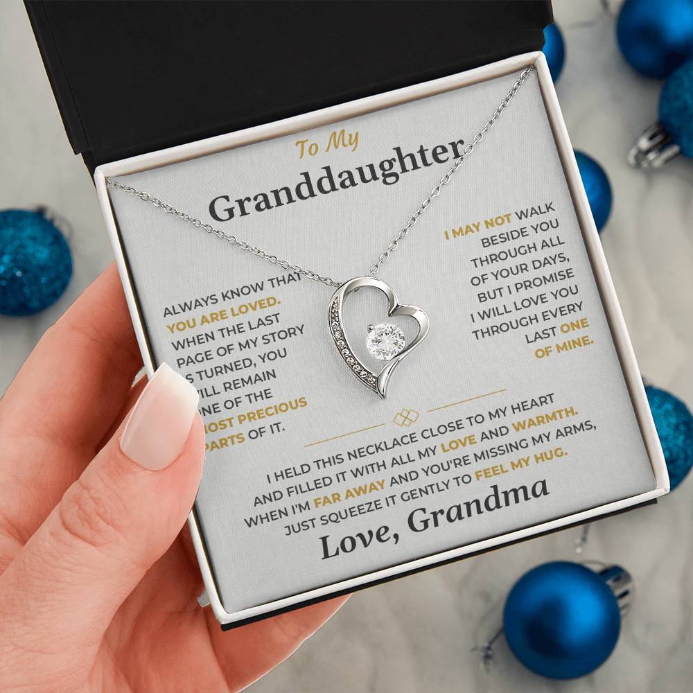 Hand holding the soft gray To My Granddaughter card from Grandma gift box by blue Christmas ornaments on white fur