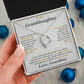 Hand holding the soft gray To My Granddaughter card from Grandma gift box by blue Christmas ornaments on white fur