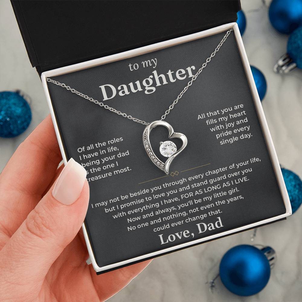 Hand holding the charcoal To My Daughter card from Dad gift box by blue Christmas ornaments on white fur