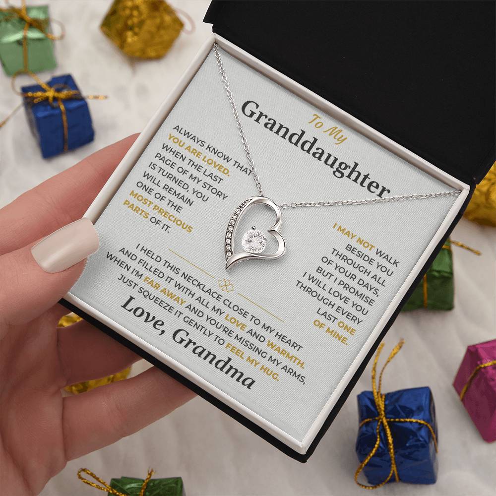 Hand holding the soft gray To My Granddaughter card from Grandma and heart necklace box among wrapped Christmas gifts