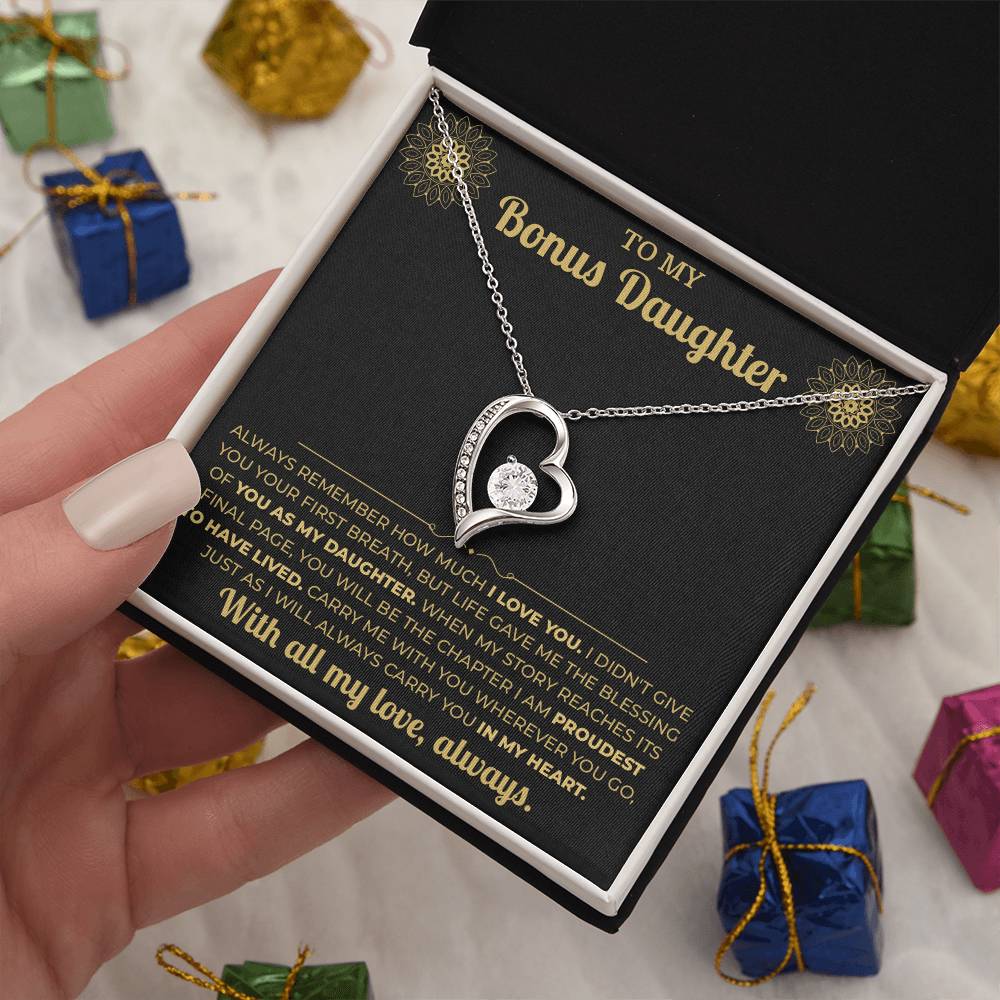 Hand holding the black and gold To My Bonus Daughter card and heart necklace box among wrapped Christmas gifts