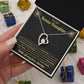 Hand holding the black and gold To My Bonus Daughter card and heart necklace box among wrapped Christmas gifts