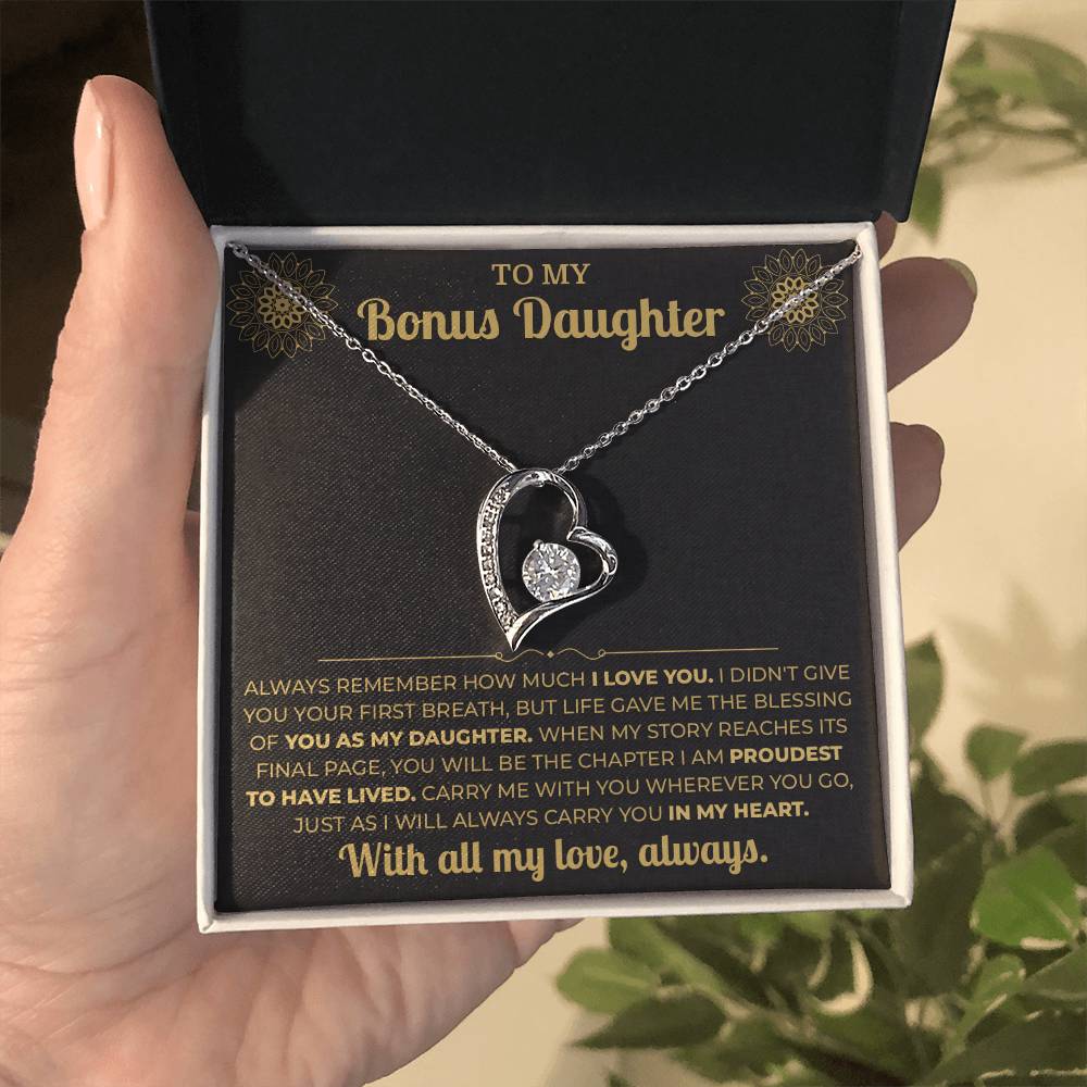 Hand holding an open black gift box with the black and gold To My Bonus Daughter card and heart pendant