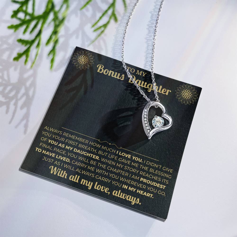 Black and gold To My Bonus Daughter card with heart necklace laid flat beside a pine sprig
