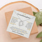 Soft gray To My Granddaughter card from Grandma with Forever Love necklace on a wood slice beside greenery