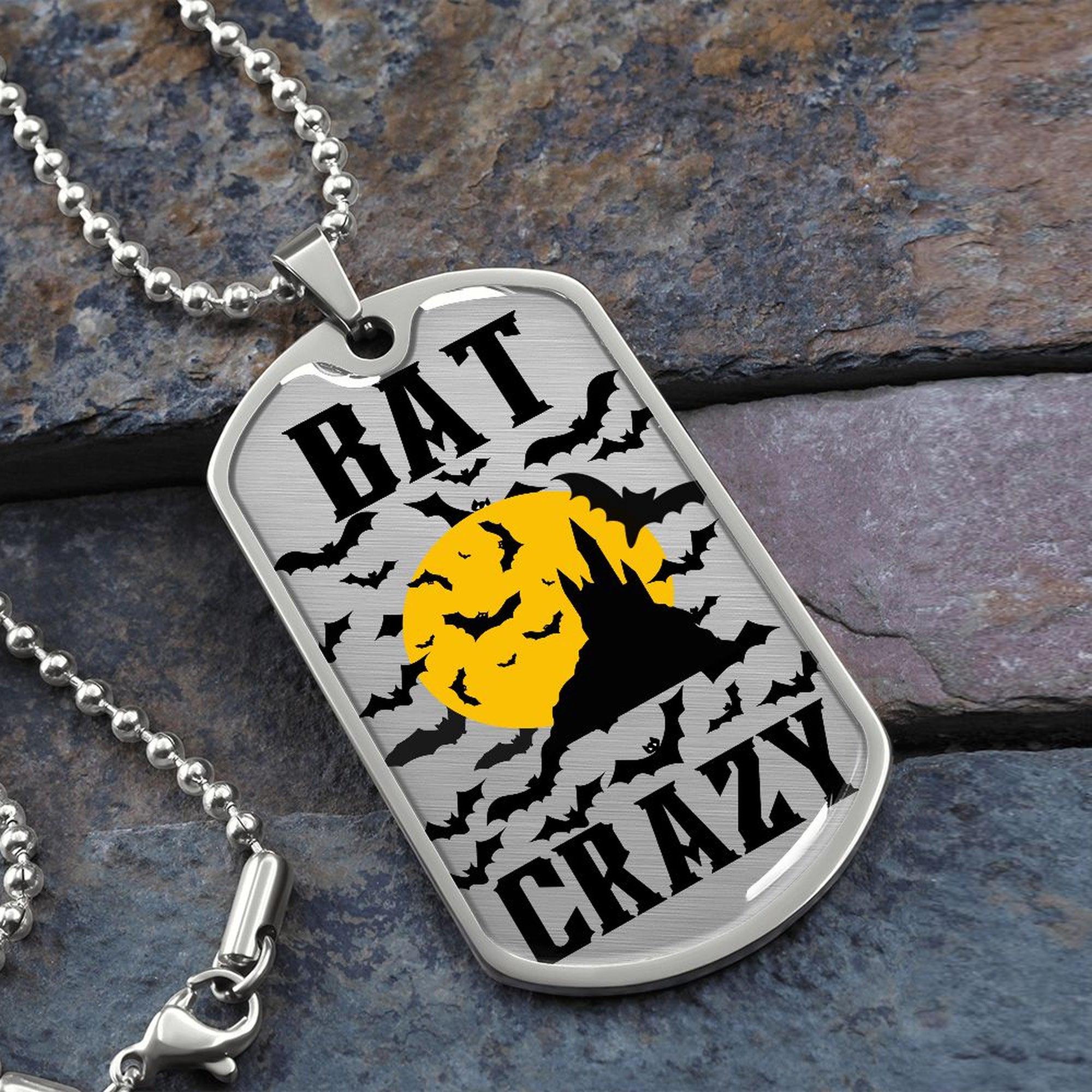 Bat Crazy bat and moon dog tag necklace in silver on a ball chain, resting on slate stone