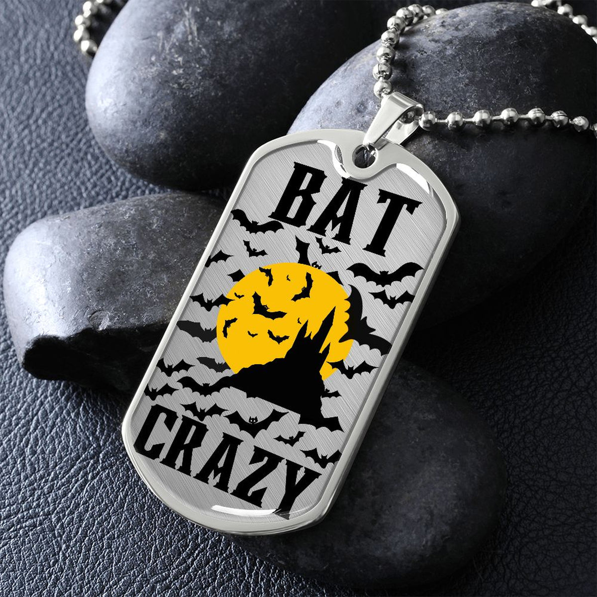 Silver Bat Crazy bat and moon dog tag necklace propped on dark river rocks