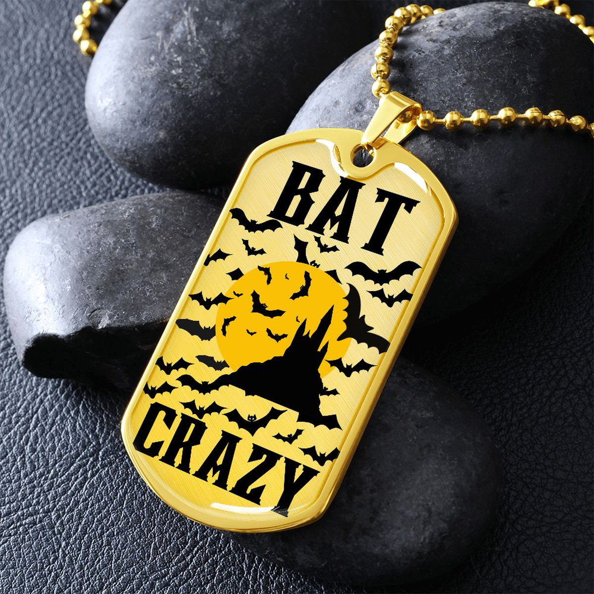 Gold-finish Bat Crazy bat and moon dog tag necklace propped on dark river rocks