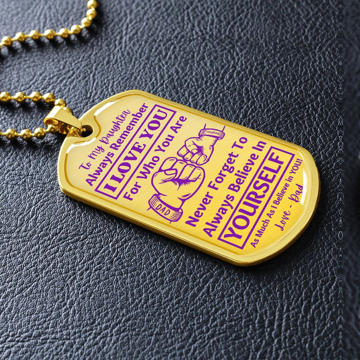 Gold-finish I Love You Daughter dog tag lying on black leather