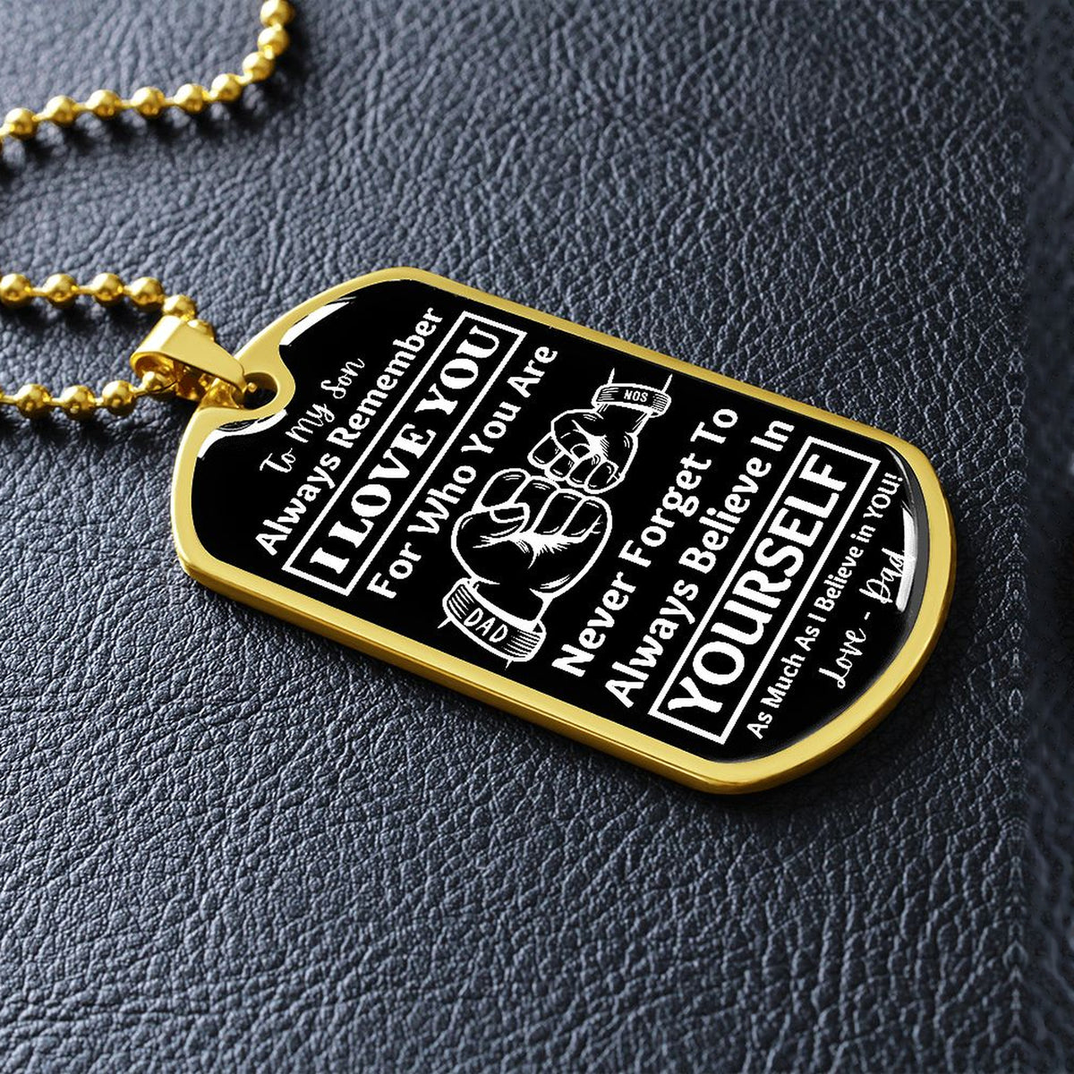 Gold-finish Believe in Yourself son dog tag lying on black leather