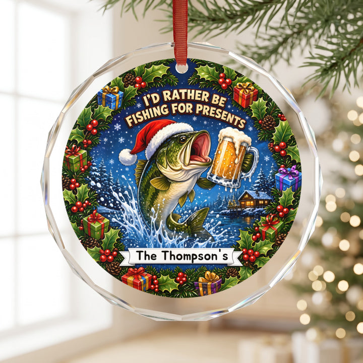 A round glass Christmas ornament hangs on a tree, featuring a bass wearing a Santa hat and holding a beer, surrounded by a festive wreath and text reading I&