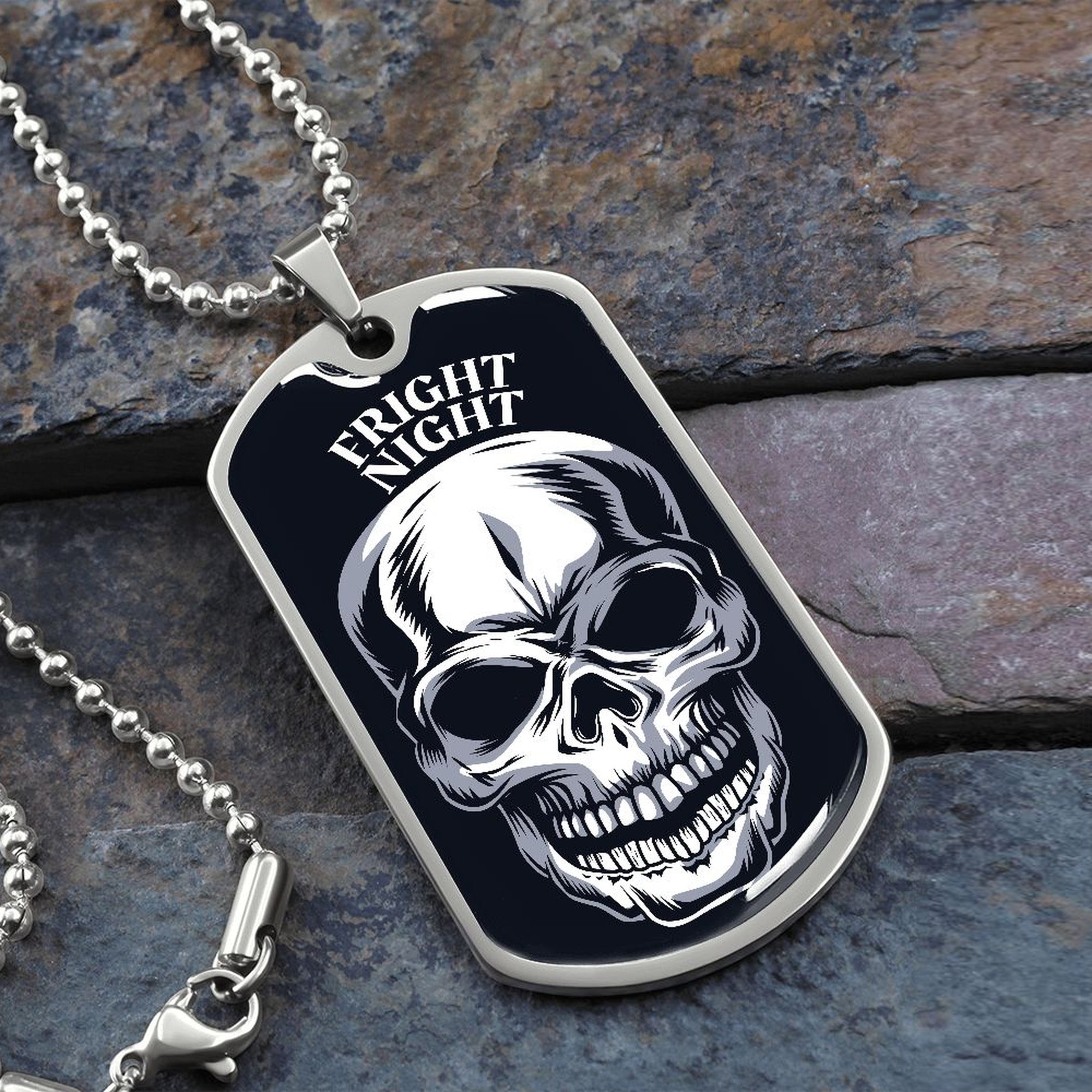 Fright Night skull dog tag necklace in silver on a ball chain, resting on slate stone