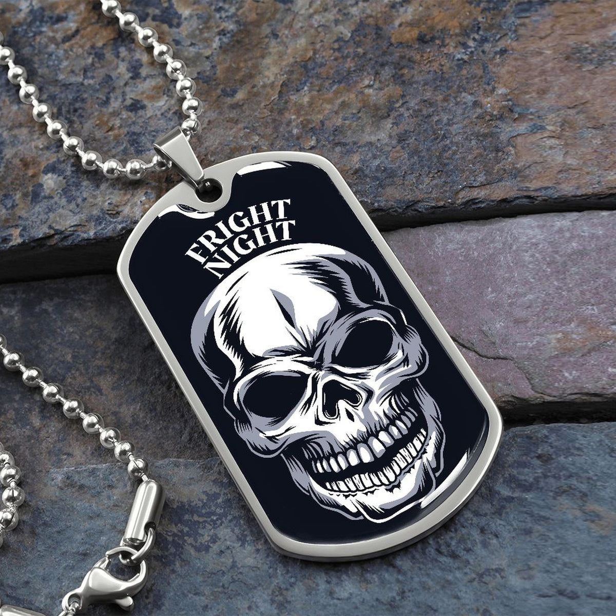 Fright Night skull dog tag necklace in silver on a ball chain, resting on slate stone