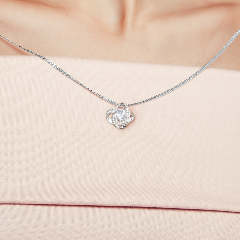 Close-up of white gold Love Knot pendant worn on blush top — oezzo