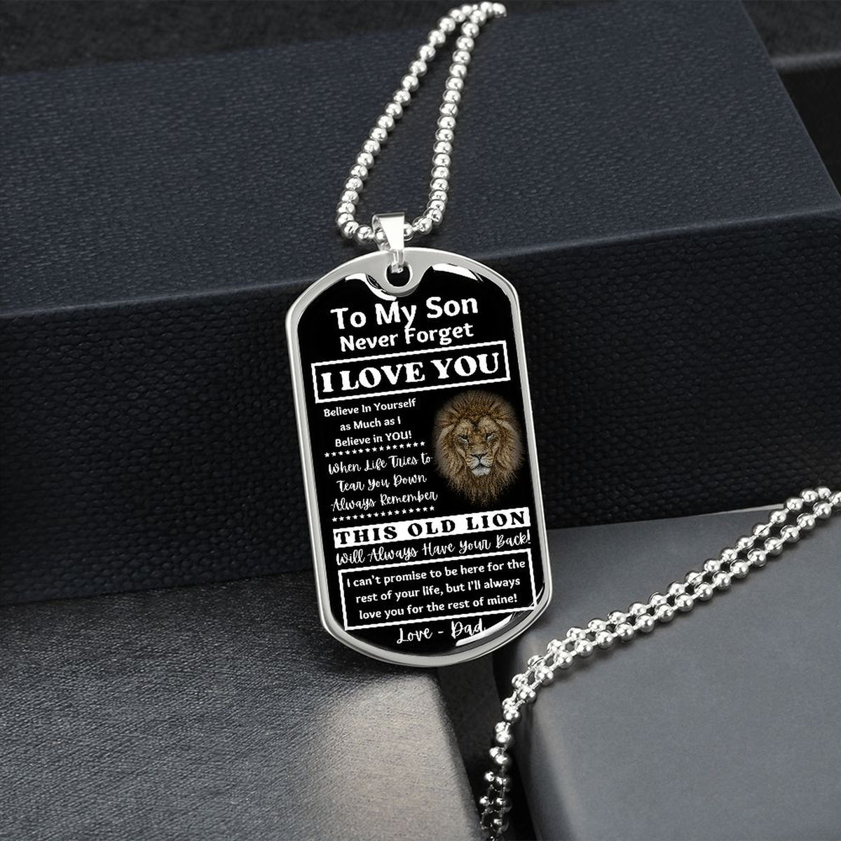 Silver Old Lion son dog tag hanging over a black gift box