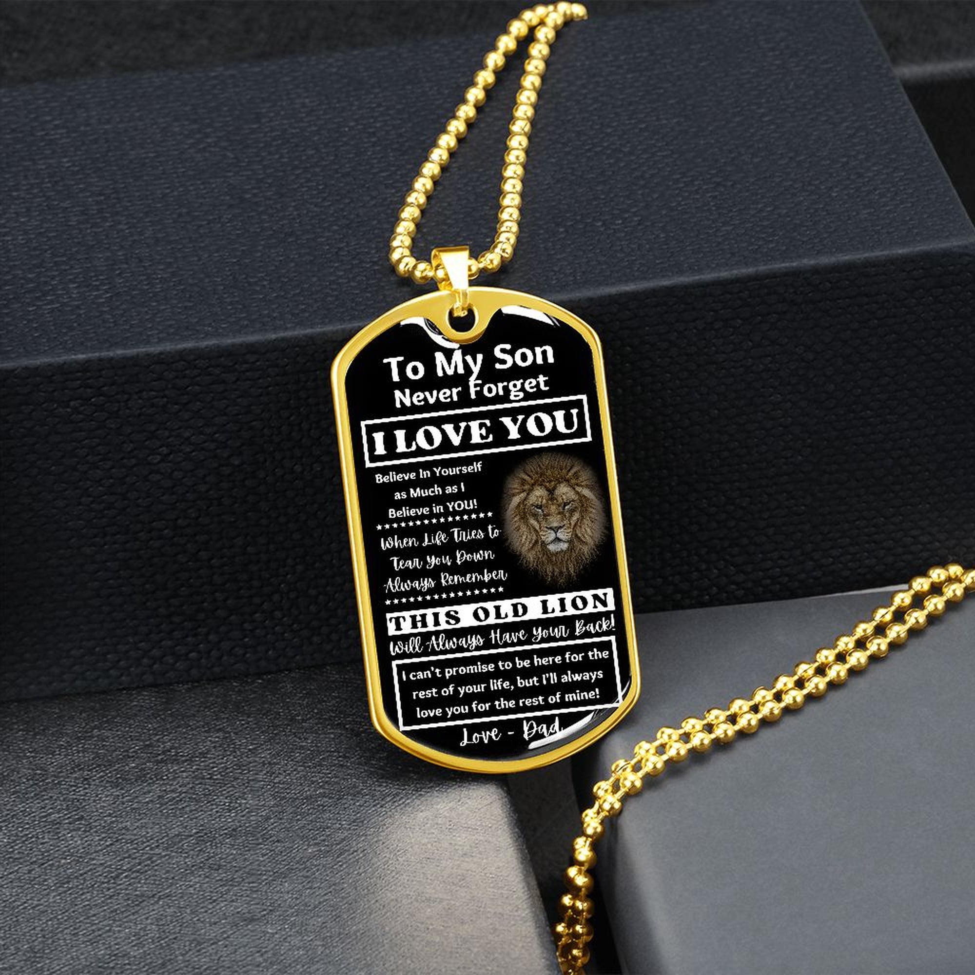 Gold-finish Old Lion son dog tag hanging over a black gift box